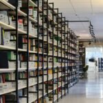 A spacious modern library with organized bookshelves and a well-lit aisle, perfect for reading and research.